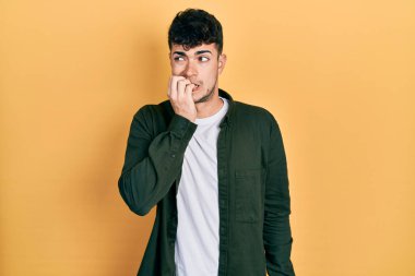 Günlük kıyafetler giyen genç İspanyol adam gergin ve gergin görünüyor. Ağzı tırnak yiyen eller. anksiyete. 