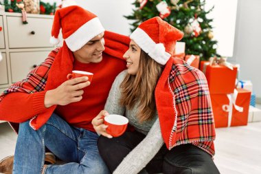 Battaniyeli Noel şapkası takan genç bir çift. Yerde oturup evde kahve içmek..