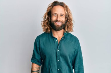 Sakallı, uzun saçlı, sıradan kıyafetler giyen ve yüzünde güzel bir gülümseme olan yakışıklı bir adam. şanslı kişi. 