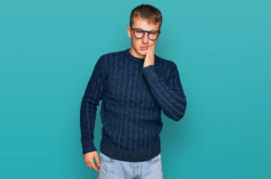 Sıradan kıyafetler giyen ve gözlüklü genç bir adam diş ağrısı ya da diş hastalığından dolayı acı dolu bir ifadeyle ağıza dokunuyor. dişçi 