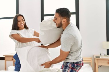 Genç Latin çift gülümsüyor. Mutlu bir şekilde evdeki yatakta yastıklarla kavga ediyorlar..