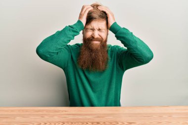 Genç İrlandalı kızıl saçlı adam masada oturmuş acı ve migrenden dolayı baş ağrısı ve stresten muzdarip. Eller başının üstünde.. 
