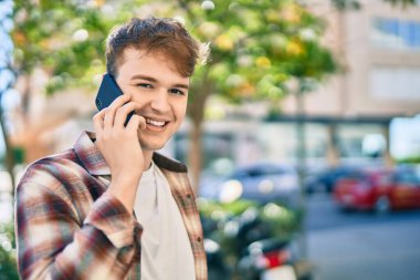 Genç beyaz adam gülümsüyor. Şehirdeki akıllı telefondan konuşuyor..