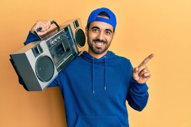 Latin kökenli genç adam müzik kutusunu tutuyor, gülümsüyor mutlu bir şekilde elleri ve parmakları kenarda işaret ediyor. 