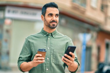 Genç İspanyol adam şehirde akıllı telefon kullanarak mutlu gülümsüyor..