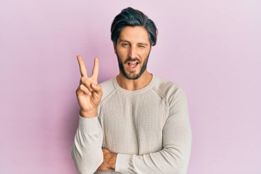 Gündelik kazak giyen genç İspanyol adam kameraya bakıp gülümseyen ve zafer işareti yapan. İki numara.. 