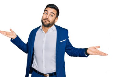 İş ceketi giyen genç bir İspanyol, elleri ve kolları havada, kafası karışık bir ifade takınıyor. şüphe kavramı. 