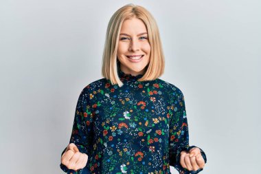 Gündelik kıyafetler giyen genç sarışın kadın çok mutlu ve heyecanlı. Kazanan jestler yapıyor. Kolları havada, gülümsüyor ve başarı için bağırıyor. kutlama konsepti. 