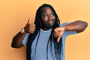 Örgülü genç siyahi kadın baş parmağını kaldırıyor ve baş parmağını kaldırıyor. Gülümsüyor ve diğer tarafa bakıyor ve düşünüyor.. 