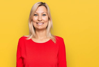 Orta yaşlı, beyaz, sıradan kıyafetler giyen mutlu ve havalı bir gülümsemesi olan bir kadın. şanslı kişi. 