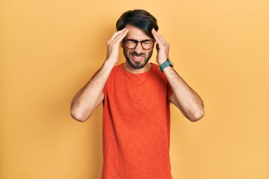 Baskı yüzünden başı ağrıyan gündelik kıyafetler ve gözlük takan genç İspanyol bir adam. migren ağrısı. 