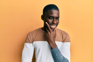 Sıradan kıyafetler giyen genç Afro-Amerikalı adam kameraya kendinden emin bakıyor kollarını kavuşturmuş ve çenesini kaldırmış gülümsüyor. Olumlu düşünmek. 