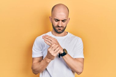 Genç kel bir adam günlük beyaz tişört giyiyor. Ellerinde ve parmaklarında ağrı var. Eklem iltihabı. 