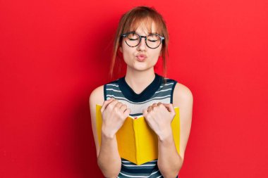 Kızıl saçlı, kitap okuyan, gözlüklü, kameraya bakıp öpüşen, güzel ve seksi bir kadın. aşk ifadesi. 