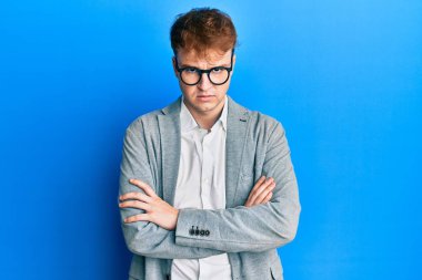 Zarif kıyafetler giyen, gözlüklü, şüpheci ve gergin genç beyaz bir adam. Yüzünde çapraz kollarla onaylamayan bir ifade var. negatif kişi. 