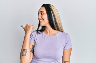 Genç İspanyol kadın gündelik giysiler giyip baş parmağını yukarı kaldırıyor ve ağzı açık gülümsüyor. 