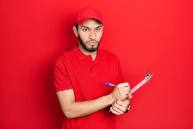 Sakallı, kurye üniformalı İspanyol adam elinde pano, yüzünde ciddi bir ifadeyle gevşemiş. Basit ve doğal bir şekilde kameraya bakıyorsun.. 