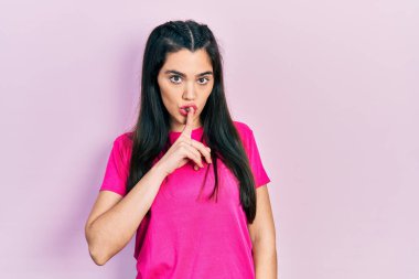 Gündelik pembe tişört giyen genç İspanyol kız dudaklarında parmaklarıyla sessiz olmak istiyor. sessizlik ve gizli konsept. 