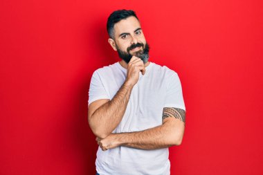 Günlük beyaz tişört giyen genç İspanyol adam kameraya kollarını kavuşturmuş ve çenesi üzerinde kendinden emin bir şekilde bakıyor. Olumlu düşünmek. 