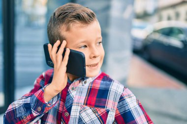 Sevimli beyaz çocuk gülümsüyor. Şehirdeki akıllı telefondan konuşuyor..