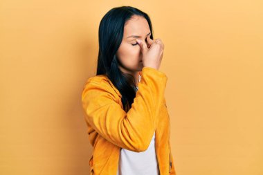 Burnu delinmiş, sarı deri ceket giyen, burnu ve gözleri ovuşturan yorgun, yorgun ve başı ağrıyan güzel İspanyol bir kadın. Stres ve hüsran kavramı. 