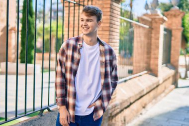 Genç beyaz adam gülümseyerek şehirde mutlu mesut duruyor..