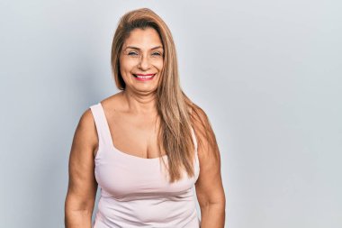 Orta yaşlı İspanyol kadın kolsuz tişörtlü, sıradan giyinmiş mutlu ve havalı bir gülümsemesi var. şanslı kişi. 