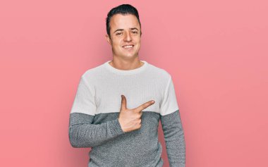 Yakışıklı, kışlık süveter giyen, neşeli, yüzünde mutlu ve doğal bir ifadeyle elleri ve parmaklarıyla yüzünü gösteren bir gülümseme olan genç bir adam. 