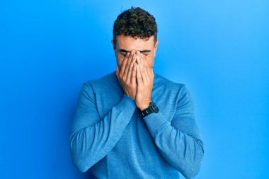 Günlük kazak giyen İspanyol genç adam yorgunluk ve baş ağrısı için gözlerini ovuşturuyor, uykulu ve yorgun ifade. görme sorunu 