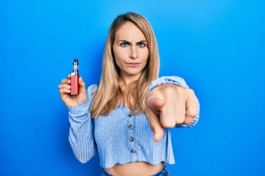 Elektronik sigara tutan genç beyaz kadın kamerayı işaret ediyor ve sen kendine güvenen ciddi bir hareket yapıyorsun. 