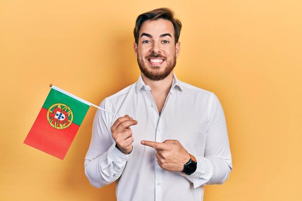 Handsome caucasian man with beard holding portugal flag smiling happy pointing with hand and finger 