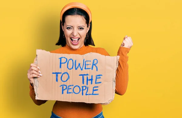 Young hispanic girl holding power to the people banner screaming proud, celebrating victory and success very excited with raised arms