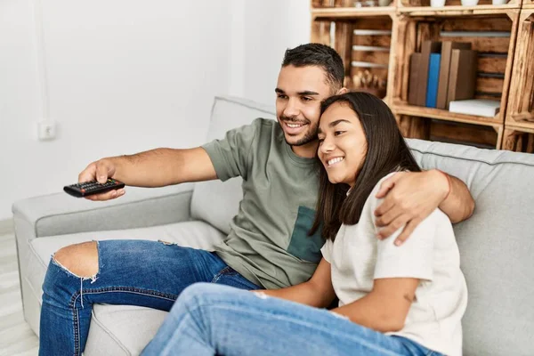 Młoda Latynoska Para Uśmiechnięta Oglądając Telewizję Domu — Zdjęcie stockowe