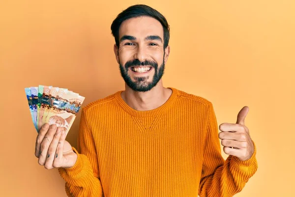 Young Hispanic Man Holding Canadian Dollars Smiling Happy Positive Thumb — Stock Photo, Image