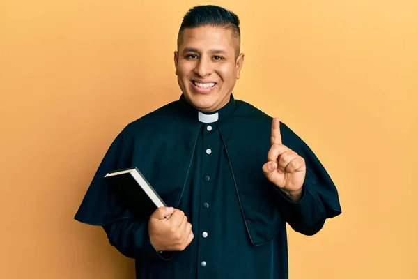 Jovem Sacerdote Latino Segurando Bíblia Sorrindo Com Uma Ideia Pergunta — Fotografia de Stock