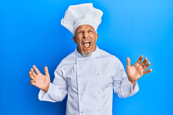 中年白发男子身穿职业厨师制服 头戴一顶疯狂的帽子 带着咄咄逼人的表情和手臂大喊大叫 沮丧的概念 — 图库照片