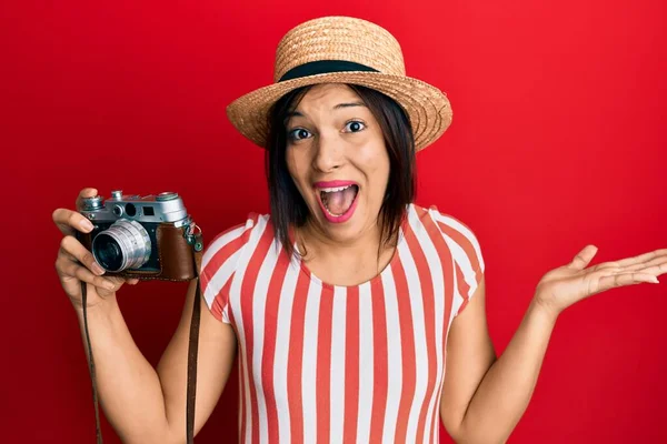 若いですラテン女性を身に着けています夏の帽子保持ヴィンテージカメラ祝い達成とともに幸せな笑顔と勝者式とともに上げ手 — ストック写真