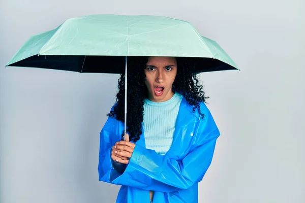 年轻的惊慌失措的女人 卷曲的头发 穿着雨衣 带着雨伞 脸上带着震惊的表情 满脸怀疑和讽刺的表情 张着嘴 吃惊极了 — 图库照片