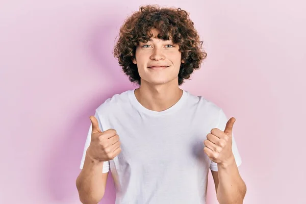 手で積極的なジェスチャーを行うカジュアルな白いTシャツの成功のサインを着てハンサムな若い男 親指を笑顔と幸せ 陽気な表情と勝者のジェスチャー — ストック写真