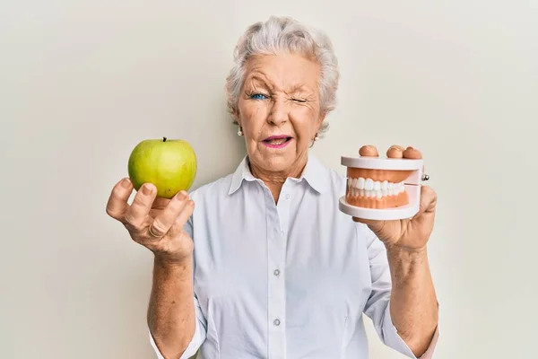 Starsza Siwowłosa Kobieta Trzyma Zielone Jabłko Zęby Protezy Mrugając Patrząc — Zdjęcie stockowe