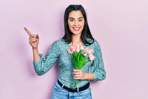 Mladý Hispánec Dívka Drží Květiny Úsměvem Šťastný Ukazuje Rukou Prstem — Stock fotografie