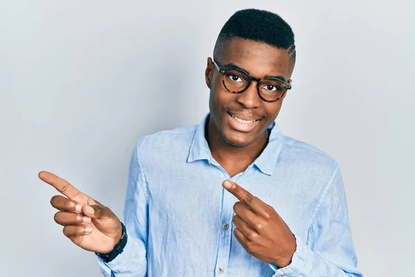 若いアフリカ系アメリカ人の男性は カジュアルな服や眼鏡を身に着けて笑顔とカメラを見て2本の手と指で側面を指して — ストック写真