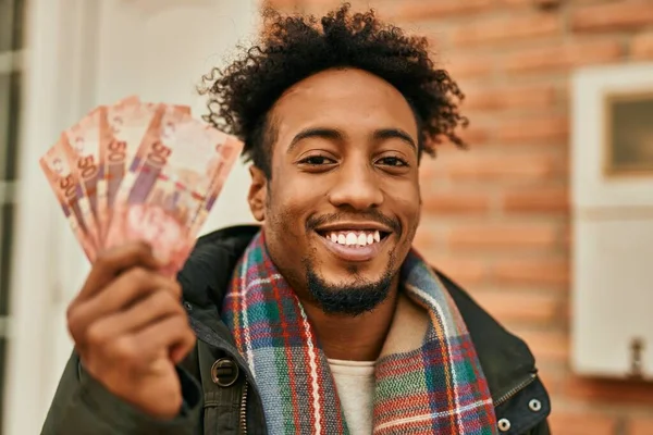 年轻的非洲裔美国人高兴地微笑着 在城里拿着南非牧场的钞票 — 图库照片