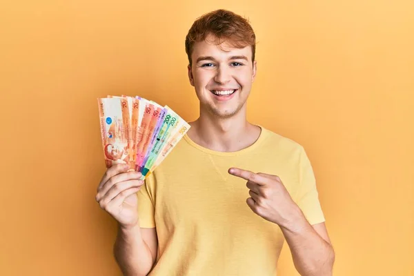 Młody Biały Mężczyzna Trzyma Philippine Peso Banknoty Uśmiechając Szczęśliwy Wskazując — Zdjęcie stockowe