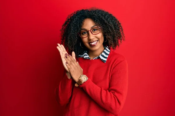 Beautiful african american woman with afro hair wearing sweater and glasses clapping and applauding happy and joyful, smiling proud hands together
