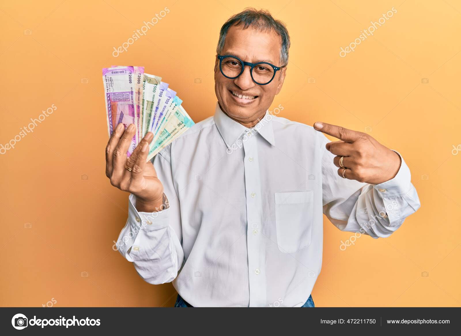 印度中年男子手持印度卢比钞票高兴地微笑着手指手画脚——图库图片© Krakenimages.com #472211750