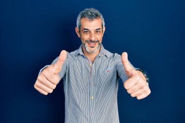 Gri saçlı, iş gömleği giyen, eli ile olumlu jest yapmayı onaylayan, gülümseyen ve başarı için sevinen orta yaşlı yakışıklı bir adam. kazanan jest. 