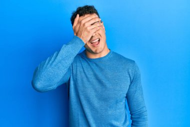 Sıradan bir kazak giyen İspanyol genç bir adam. Gülümsüyor ve elleri yüzlerinde, şaşkınlıktan gözleri kapayarak gülüyor. kör kavram. 