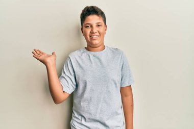Gündelik gri tişört giyen genç İspanyol çocuk neşeli bir şekilde gülümsüyor ve avuç içiyle kameraya bakıyor.. 