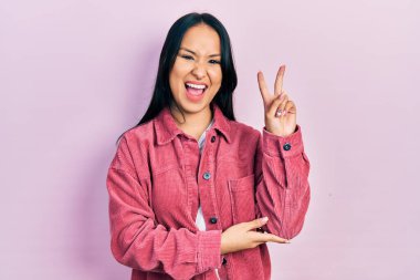 Güzel İspanyol bir kadın, burun piercingli, sıradan pembe bir ceket giyen, kameraya gülümseyen, zafer işareti yapan. İki numara.. 